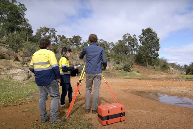 Three surveyors with a theodolite standing in a clearing in bushland